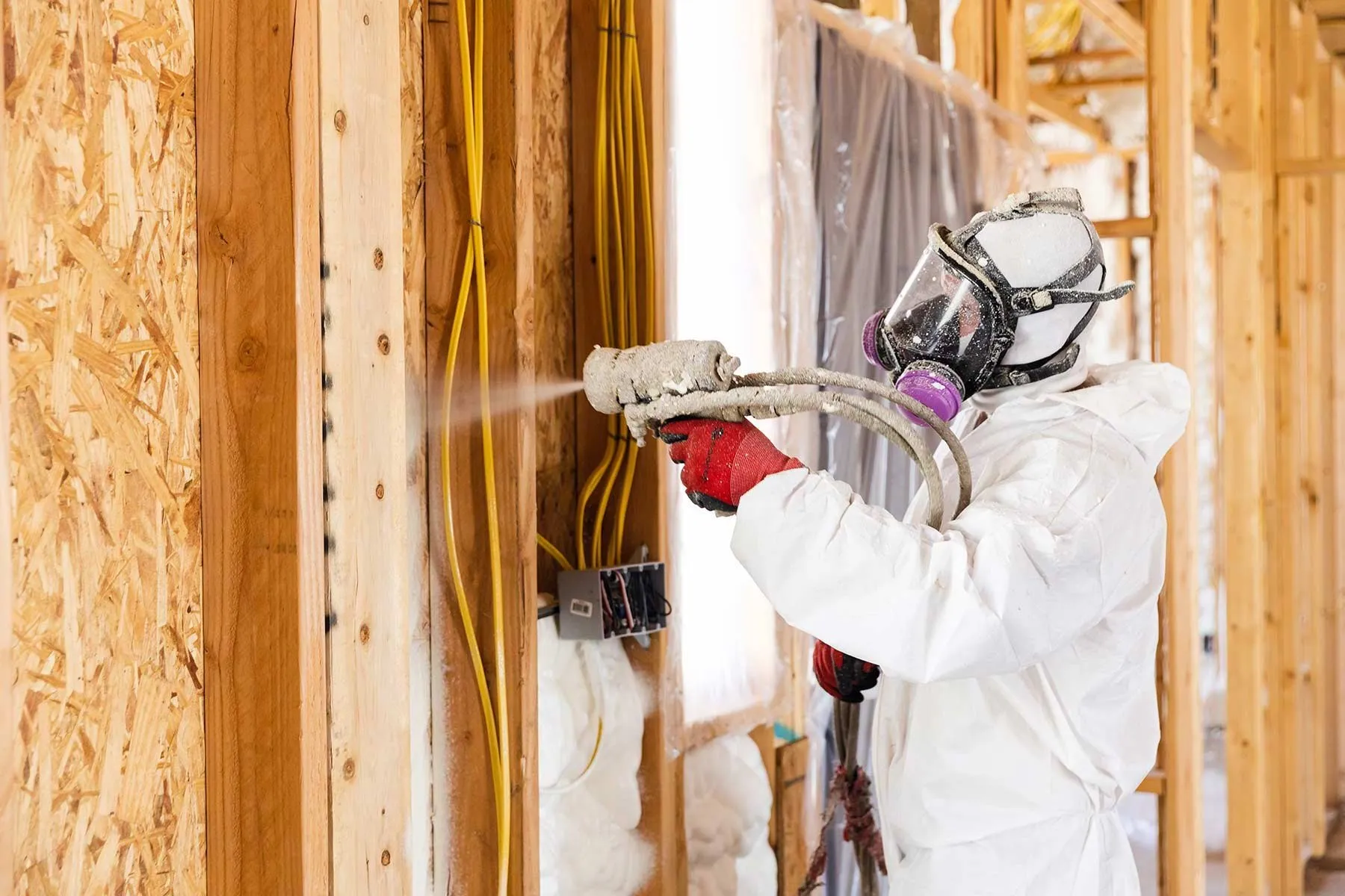 Installer spraying foam into open wall framing around wiring